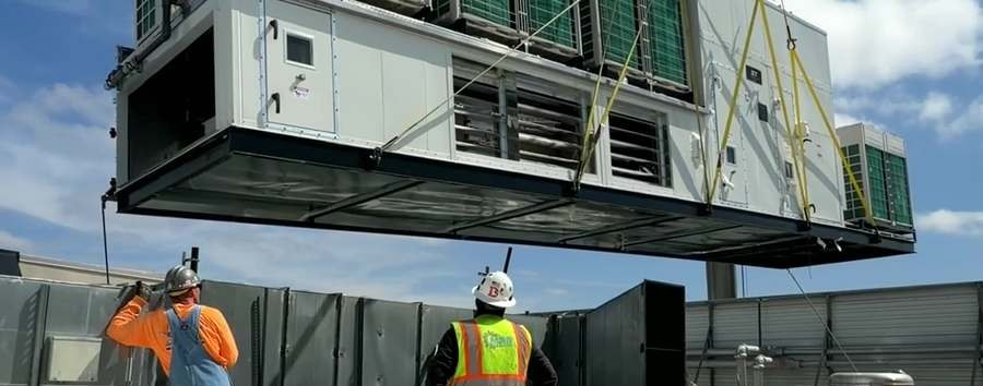 Packaged rooftop air handling unit being lifted into place by crane during installation