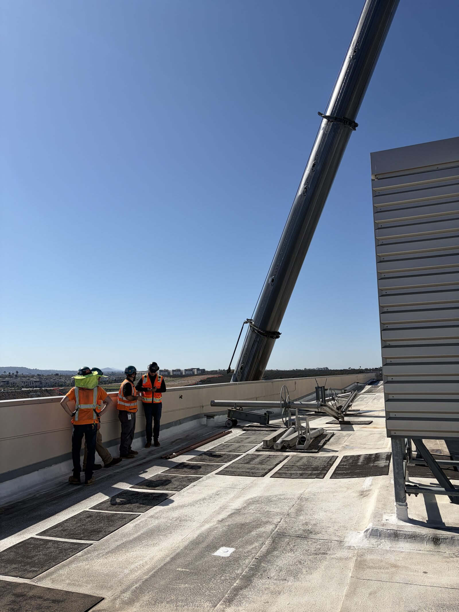 Crane and flatbed staged alongside an occupied office building for a rooftop unit changeout