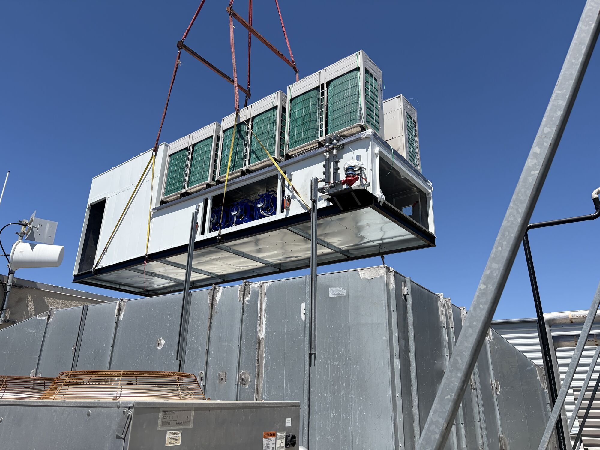 All-electric replacement rooftop unit flying over an occupied building on a crane