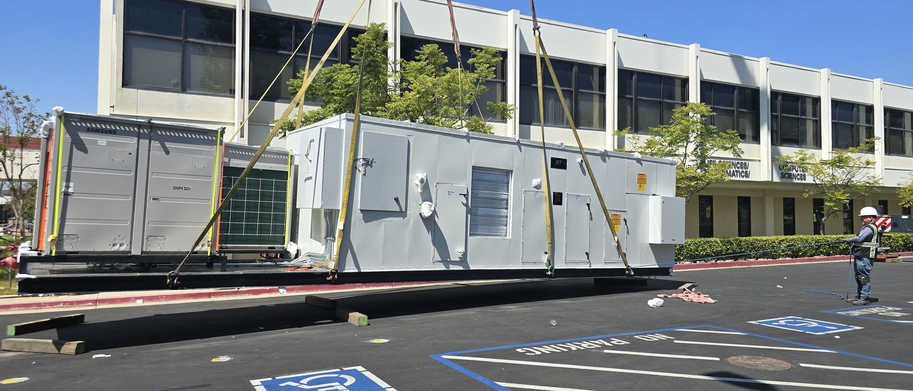 Two all-electric replacement rooftop units staged in the parking lot of an occupied office building before the lift